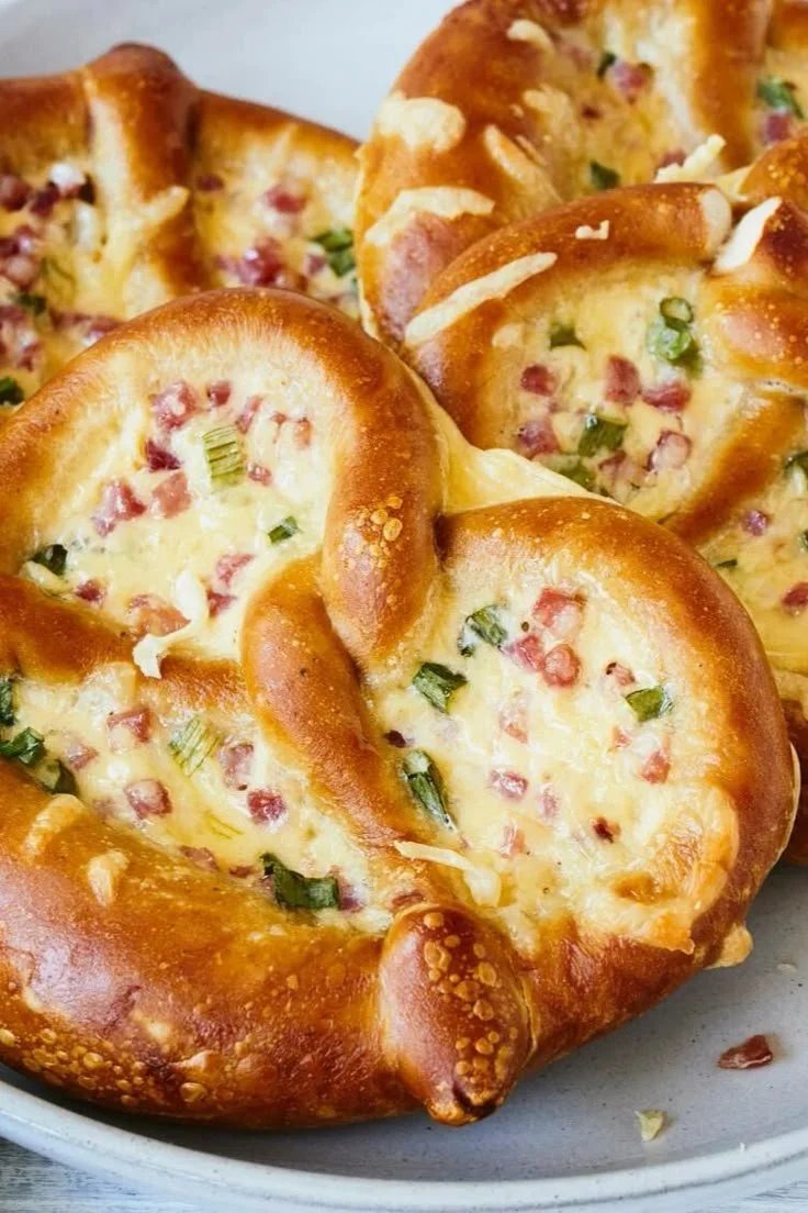 Leckere Flammkuchen-Brezeln mit herzhaften Belägen auf einem Holzbrett.